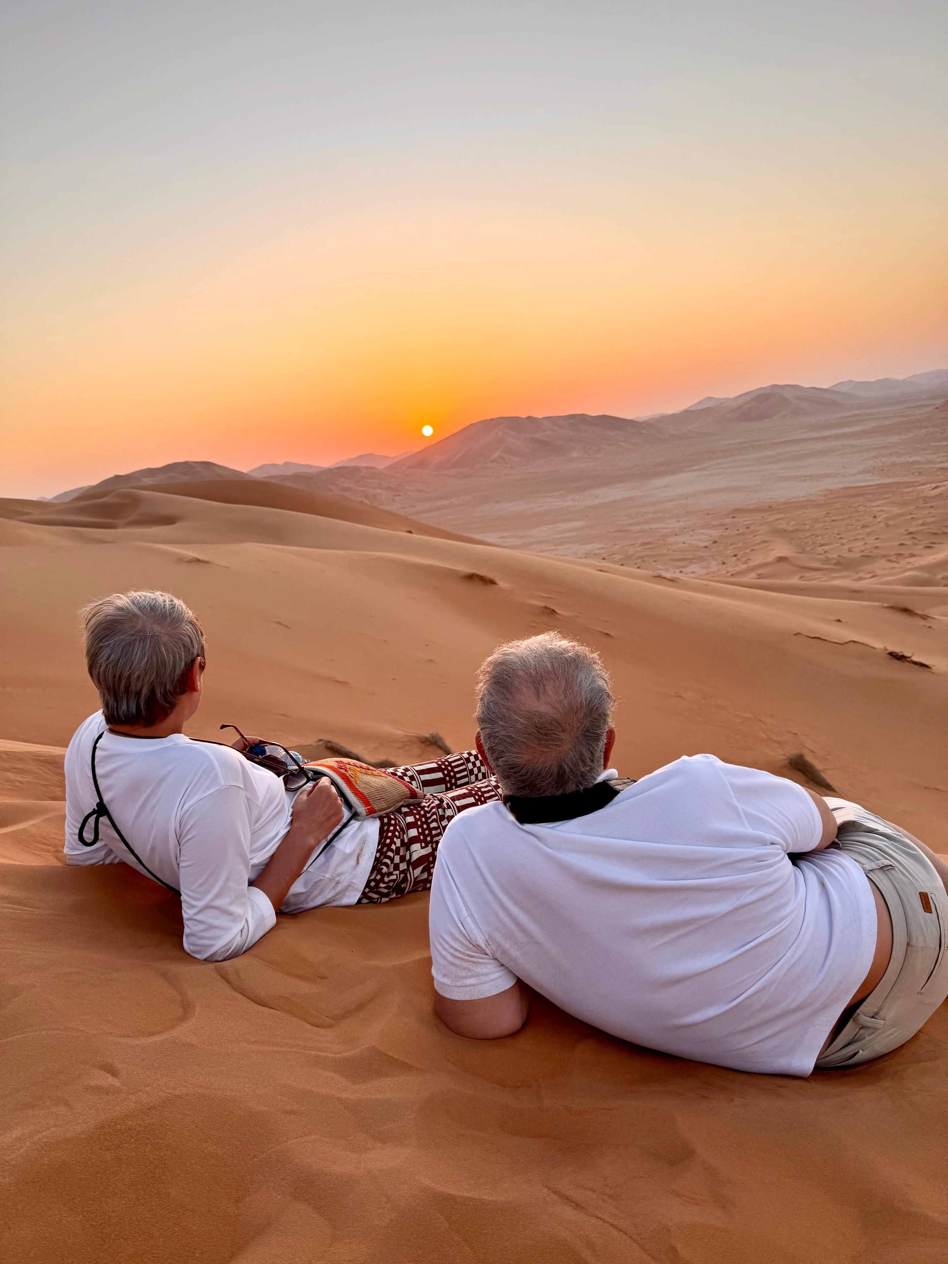 Two people on desert dunes watching sunset